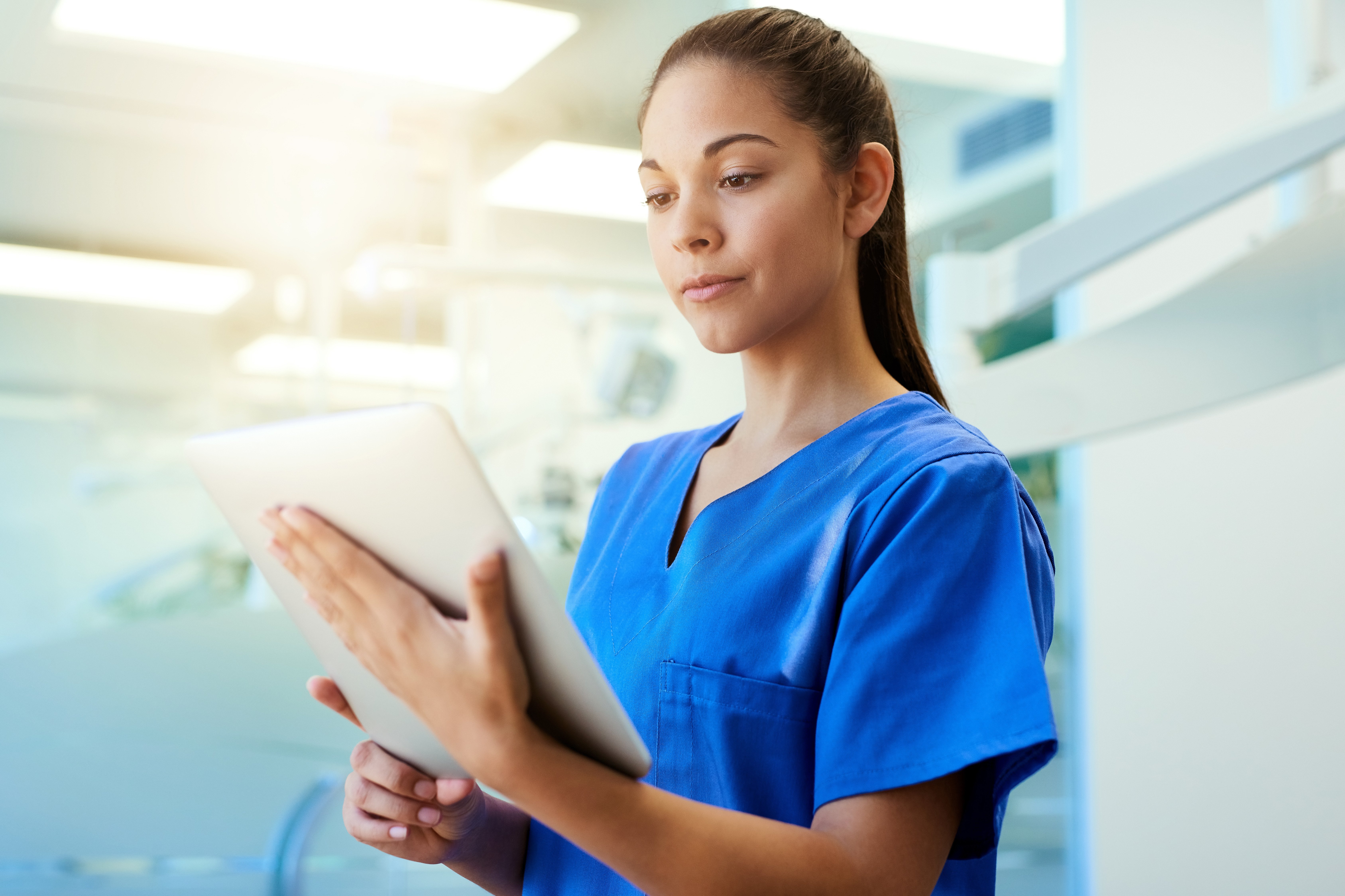 Image of a young nurse using a tablet while standing inside a clinic. 